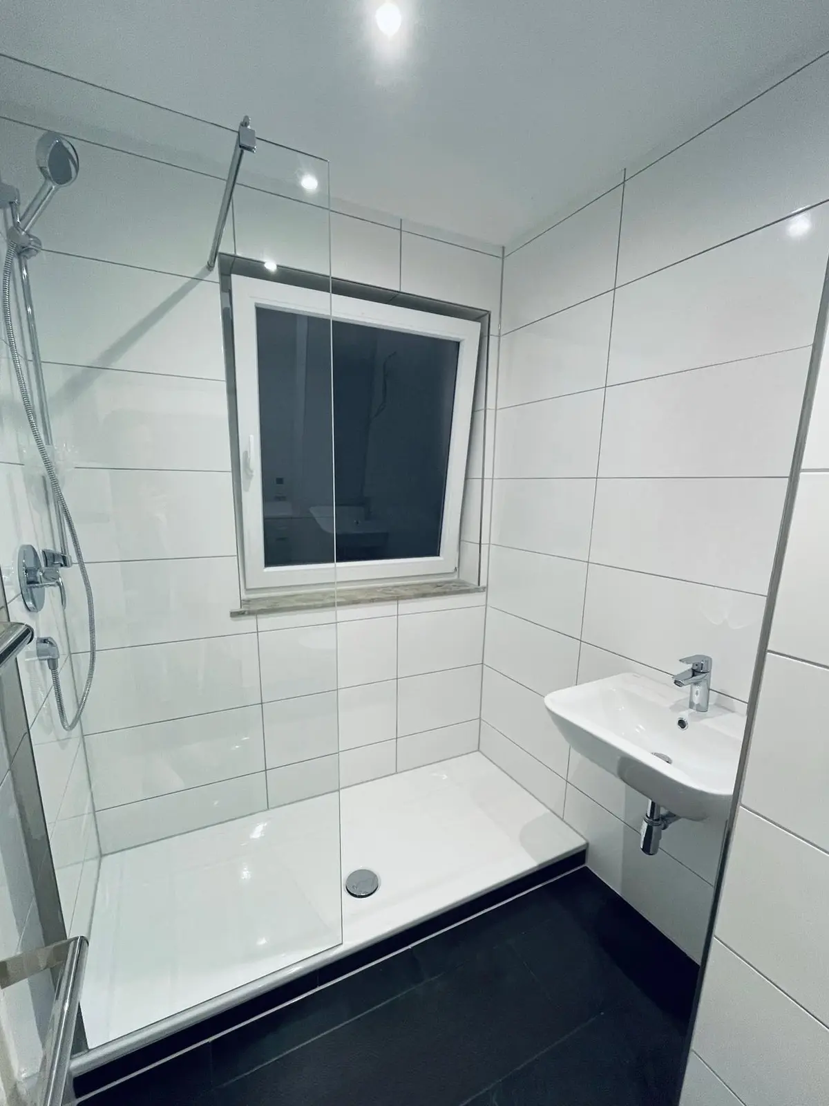Nachher: dieselbe Baustelle nach der Kernsanierung — Walk-in-Dusche mit Glaswand und neuem Waschtisch